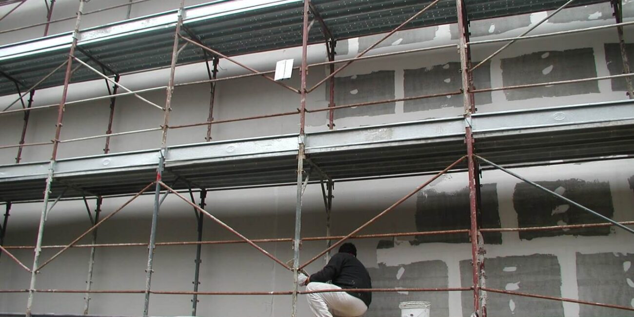 operaio sul ponteggio esegue fase di finitura tinteggiata di rivestimento modulare di facciata in fibrocemento